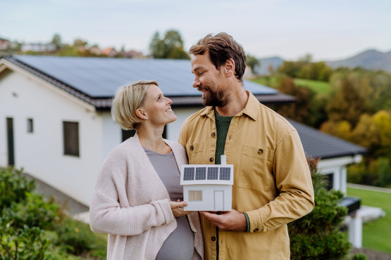 Ein Mann und eine Frau schauen sich glücklich an und halten dabei ein kleines Modell eines Hauses in der Hand.