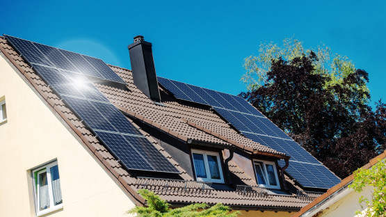 Ein Hausdach auf dem Solarpaneele montiert sind. Die Sonne spiegelt sich darin.