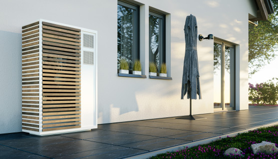 Wärmepumpen-Außeneinheit mit Holzlamellen an Wohnhauswand, Terrasse mit Sonnenschirm.
