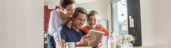 Familie in der Küche die gemeinsam auf ein Tablet schauen