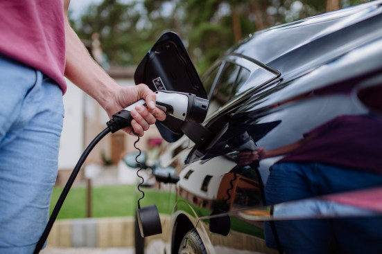 Mythen über Elektromobilität Ein Mann steckt den Stecker in ein Elektroauto, um es aufzuladen.