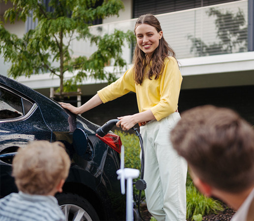 Fröhliche Familie mit kleinem Sohn wartet zusammen bis das Elektroauto geladen ist. 