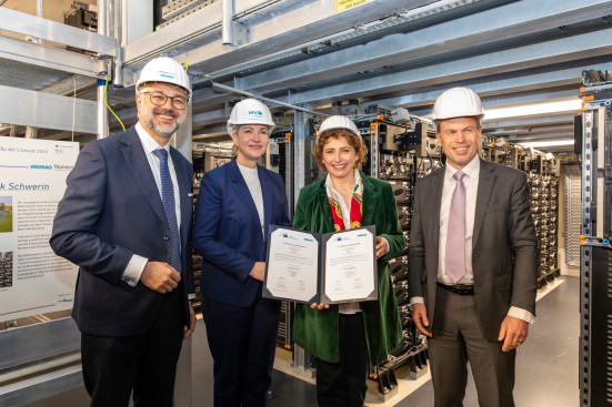 Alle Beteiligten halten im Batterieraum des Speichers den Vertrag sichtbar in den Händen.