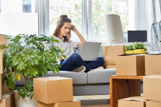 Person sitzt beim Einzug in die neue Wohnung auf dem Sofa und nutzt einen Laptop.
