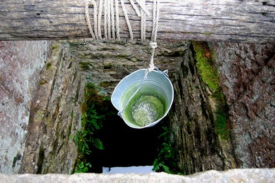 Können Fracking Chemikalien das Grundwasser verunreinigen? Alter Ziehbrunnen aus dem gerade ein Eimer Wasser nach oben geholt wird