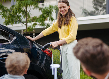 Fröhliche Familie mit kleinem Sohn wartet zusammen bis das Elektroauto geladen ist. 
