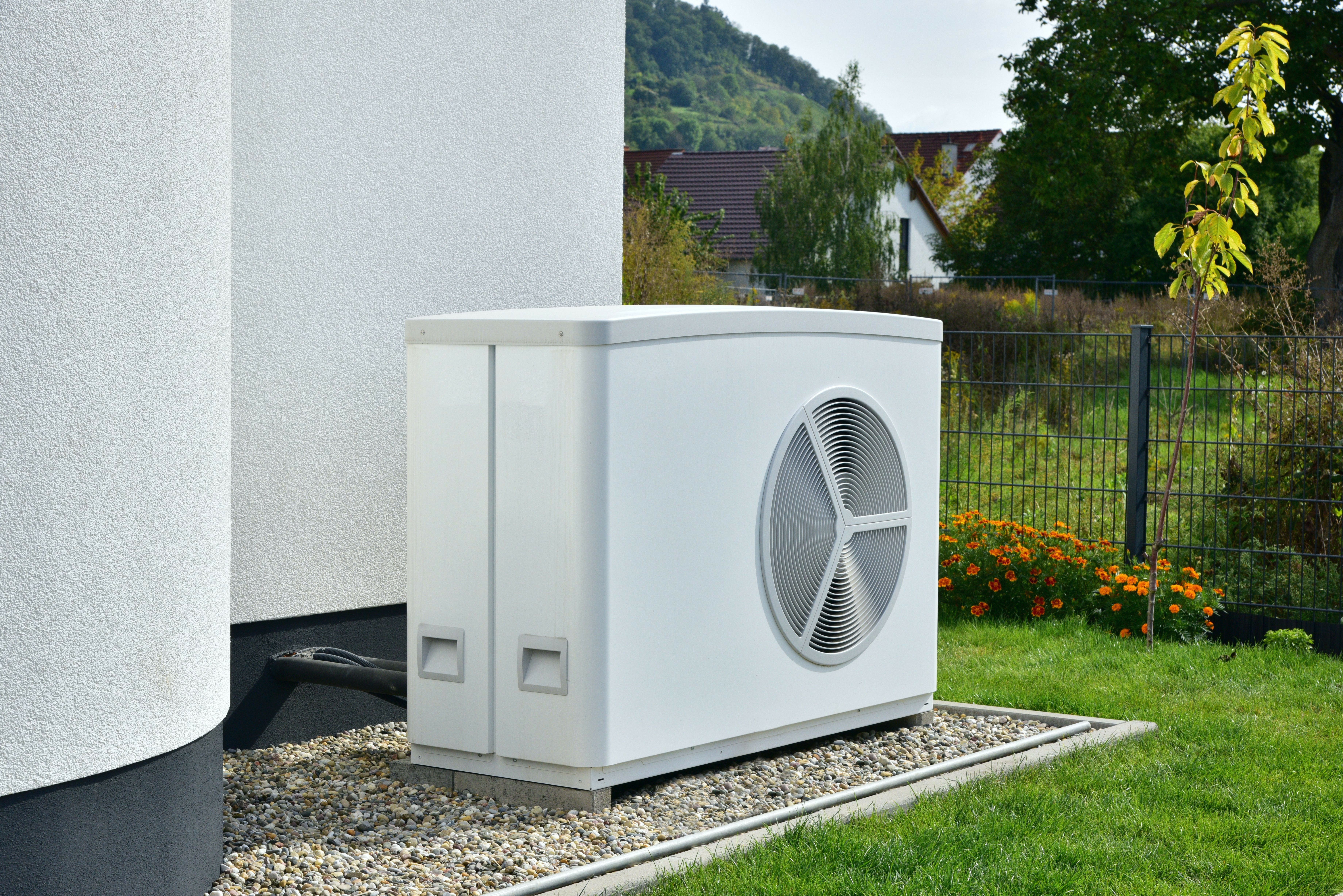 Wärmepumpe im Außenbereich eines Hauses, umgeben von Garten und Hecke. Sie spielt eine wichtige Rolle in der Heiztechnik.